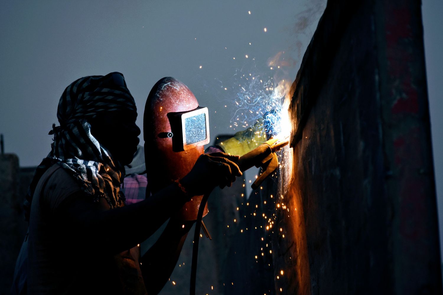 Welder in a hood and gloves running a weld on structural steel plate